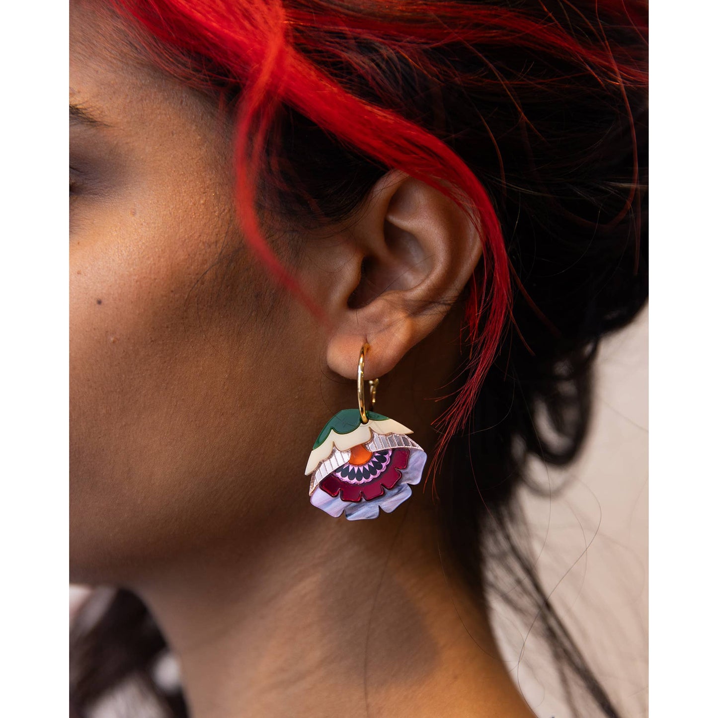 Close-up of a person wearing a colorful floral earring with red hair.
