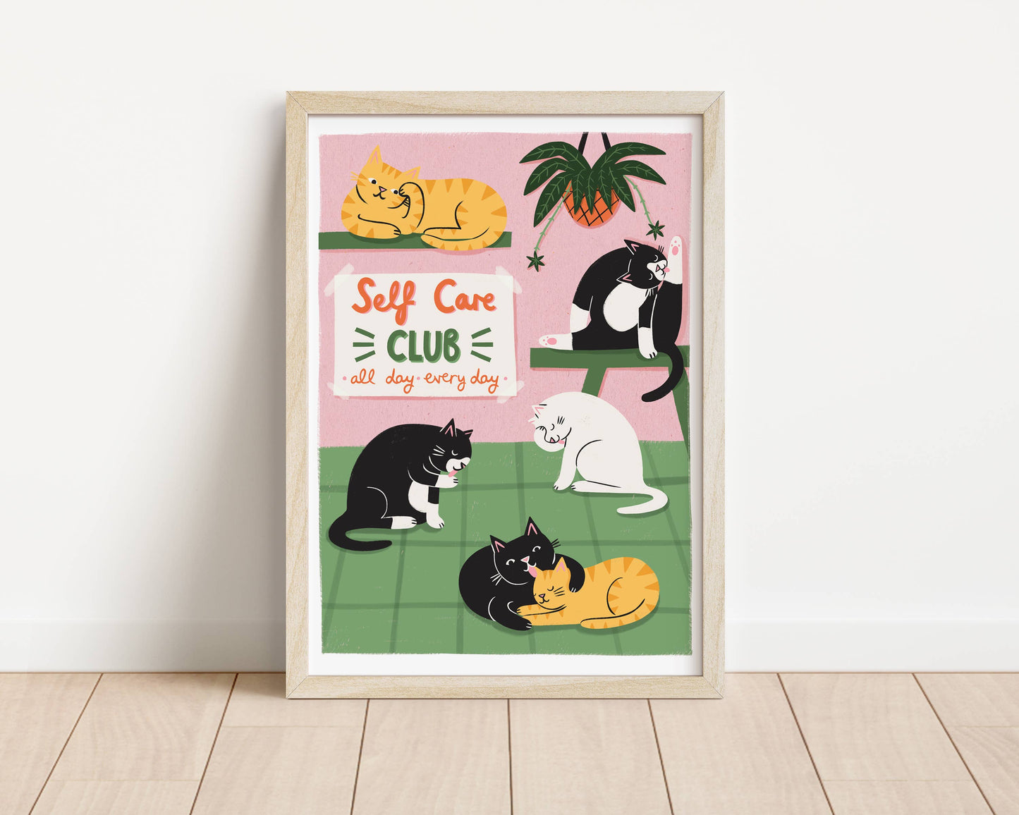 Framed artwork with cats and 'Self Care Club' text on a pink and green background