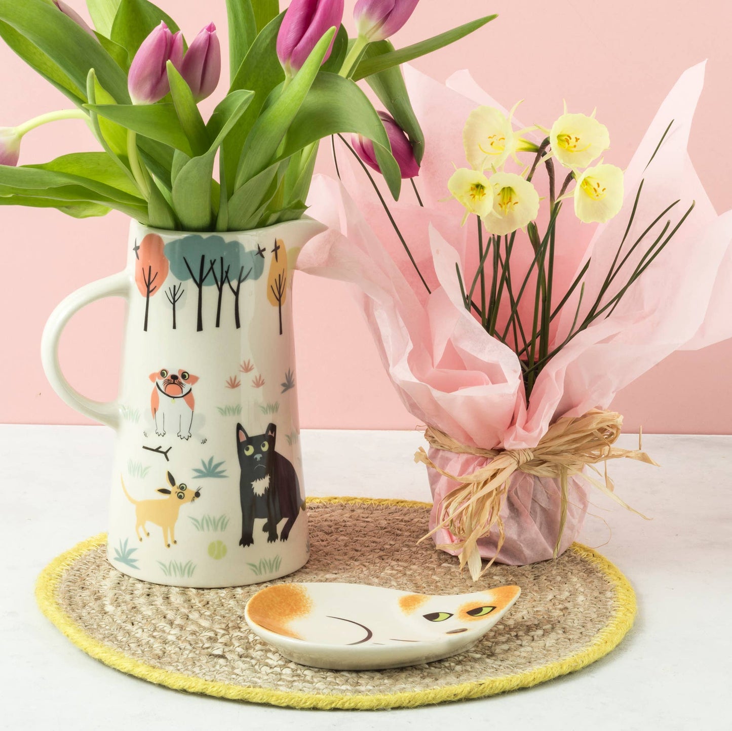 Decorative mug with floral design, small plant, and cat-shaped dish on a pink background