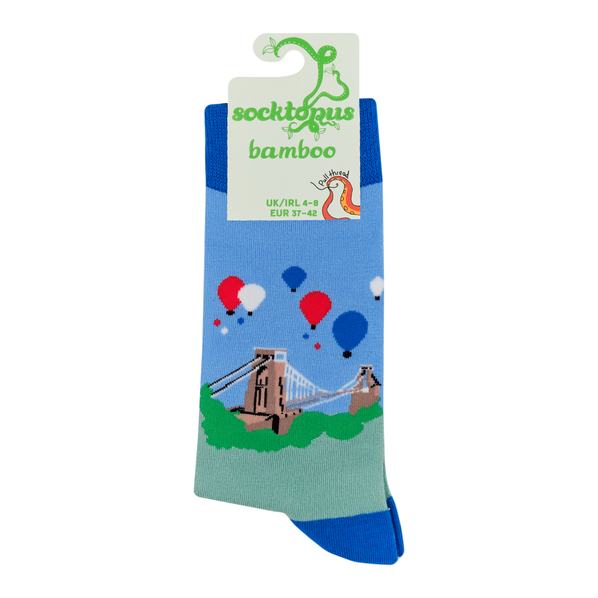 A pair of bamboo crew socks in a blue and green landscape design with a suspension bridge, hot air balloons, and a unicorn graphic on the packaging card.
