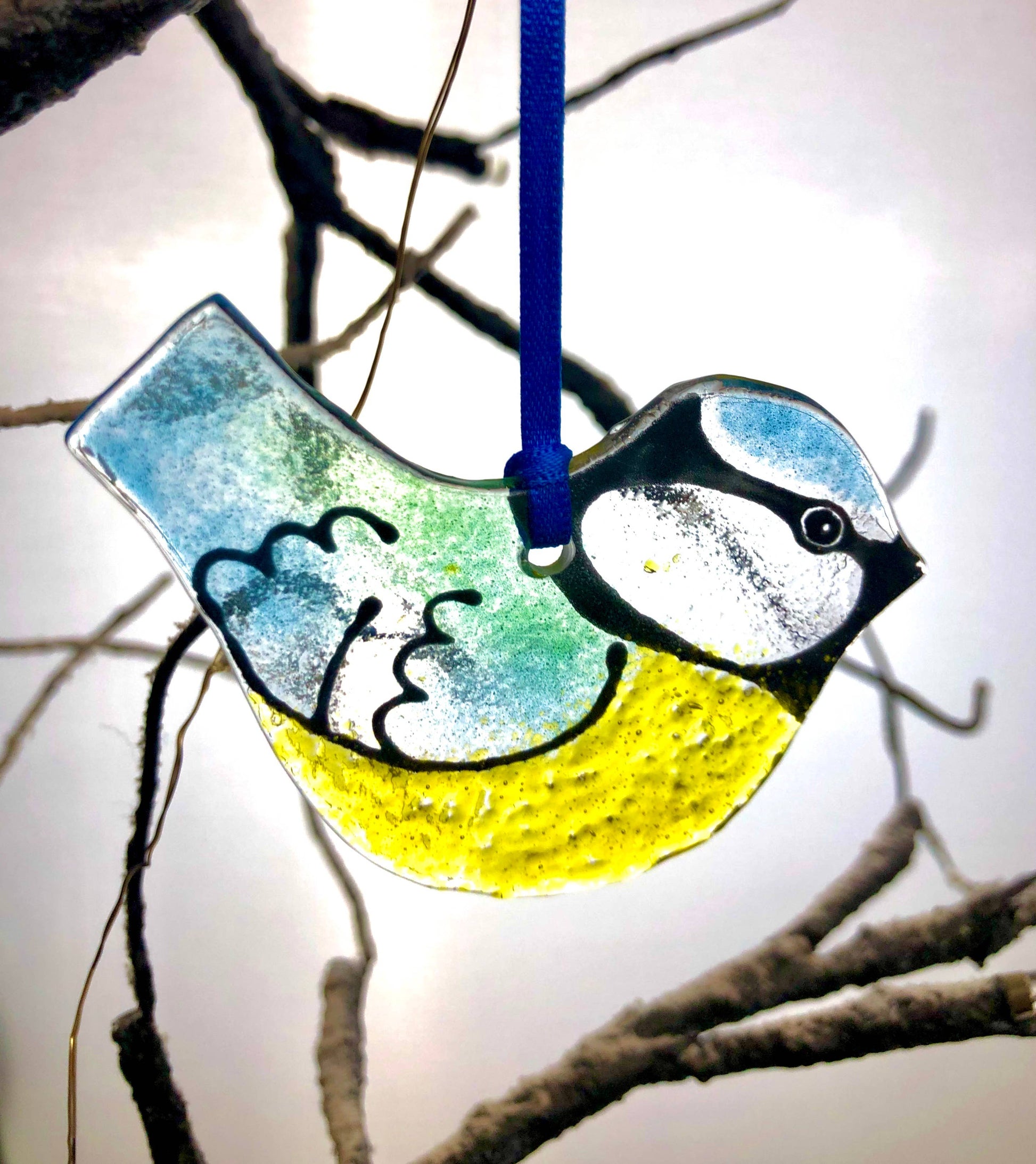 Decorative glass bird ornament hanging on a branch against a light background