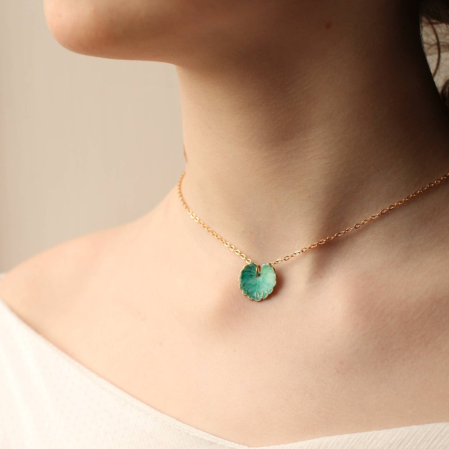 Necklace with a green pendant worn by a person on a neutral background