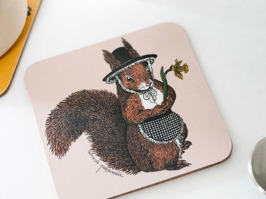 A square coaster with rounded corners featuring an illustration of a red squirrel wearing a black hat and a checkered apron, holding a daffodil.