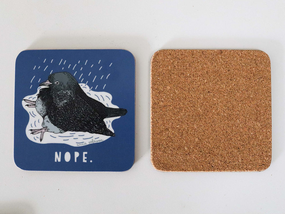 A square blue coaster with a pigeon illustration sitting in a puddle with the word 'NOPE.' underneath. To the right of the coaster is another coaster upside down, showing the cork backing.