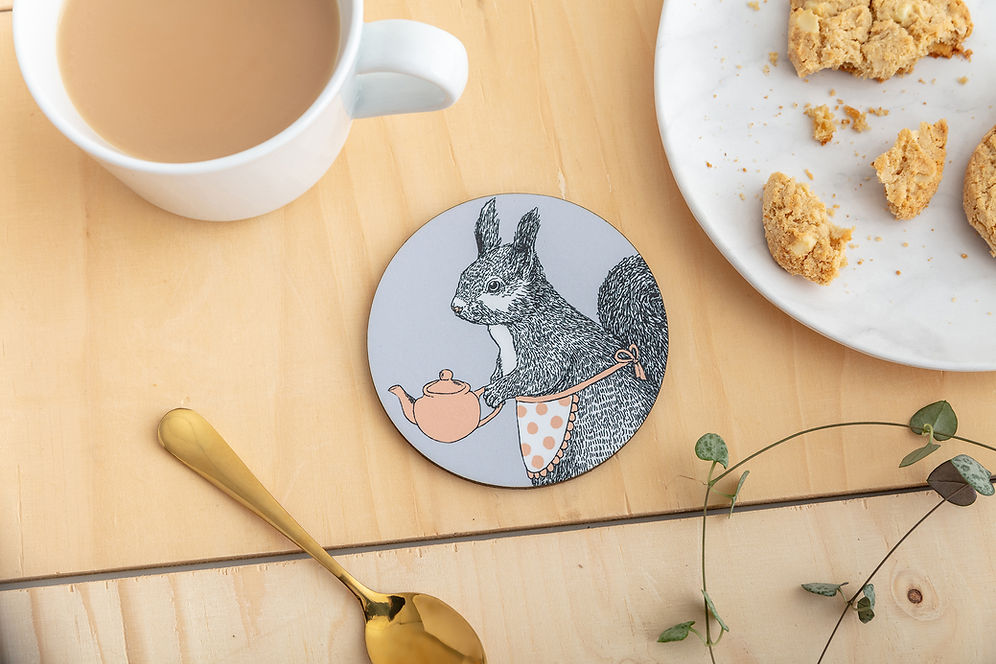 A round coaster featuring an illustration of a grey squirrel in a little apron holding a pink teapot.