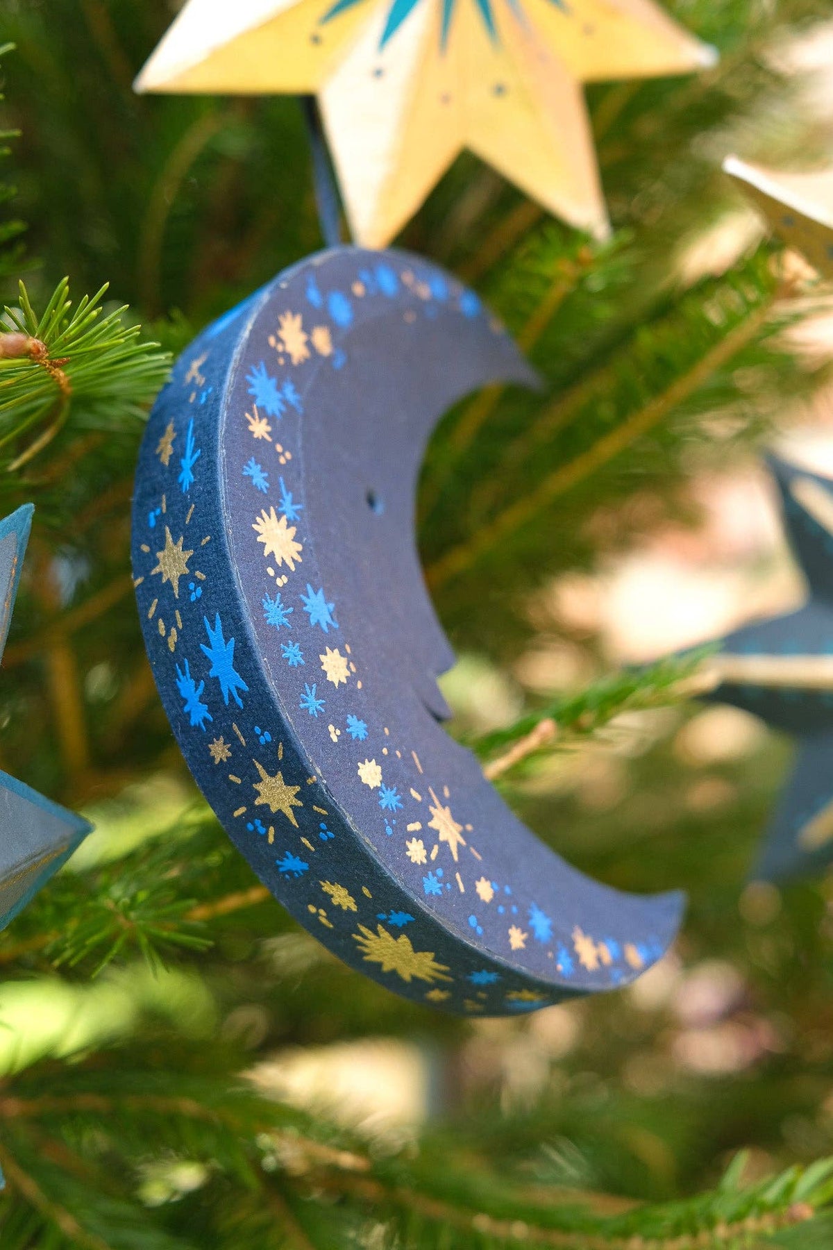 Decorative moon ornament with star patterns hanging on a Christmas tree.