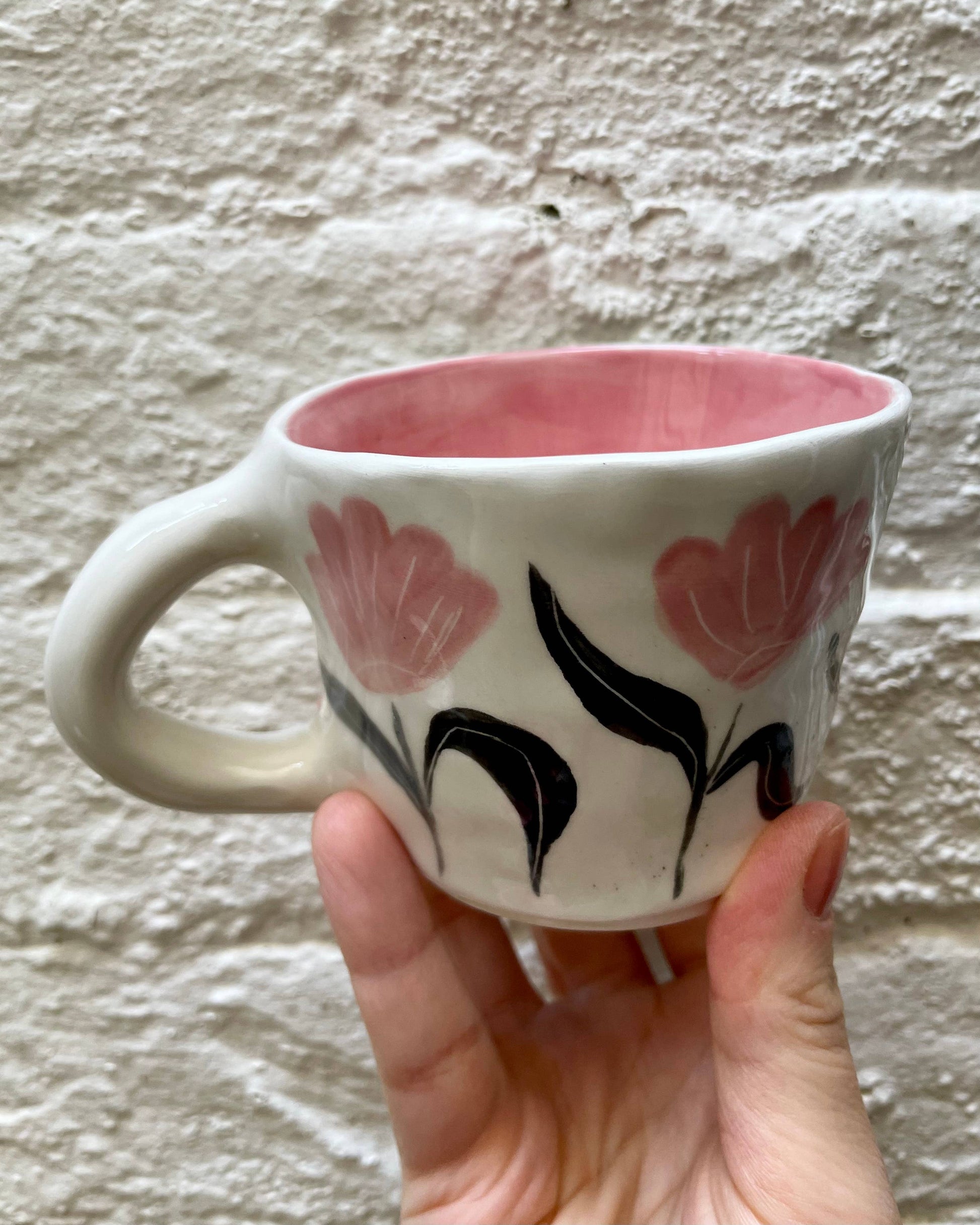 Ceramic mug with floral design held against a textured wall.