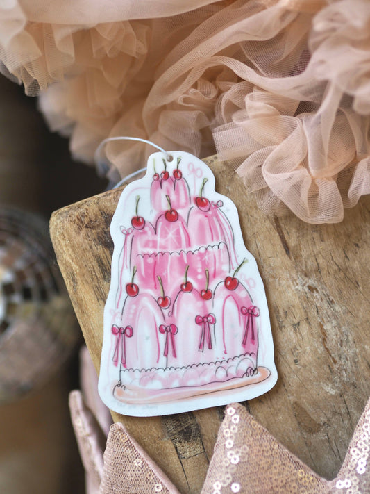 Sticker of a pink cake with cherries on a wooden surface