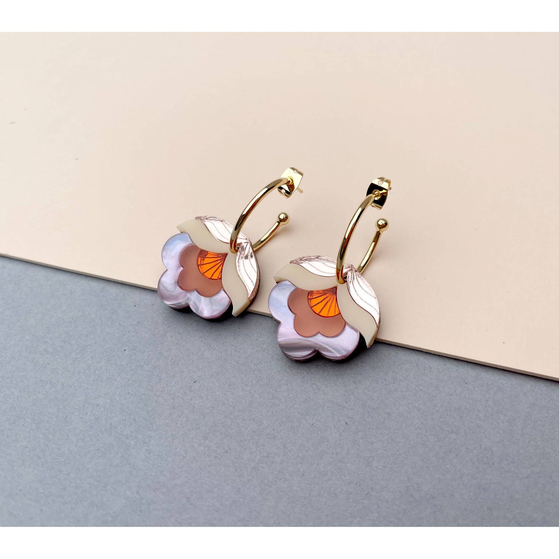 Gold hoop earrings with floral designs on a neutral background