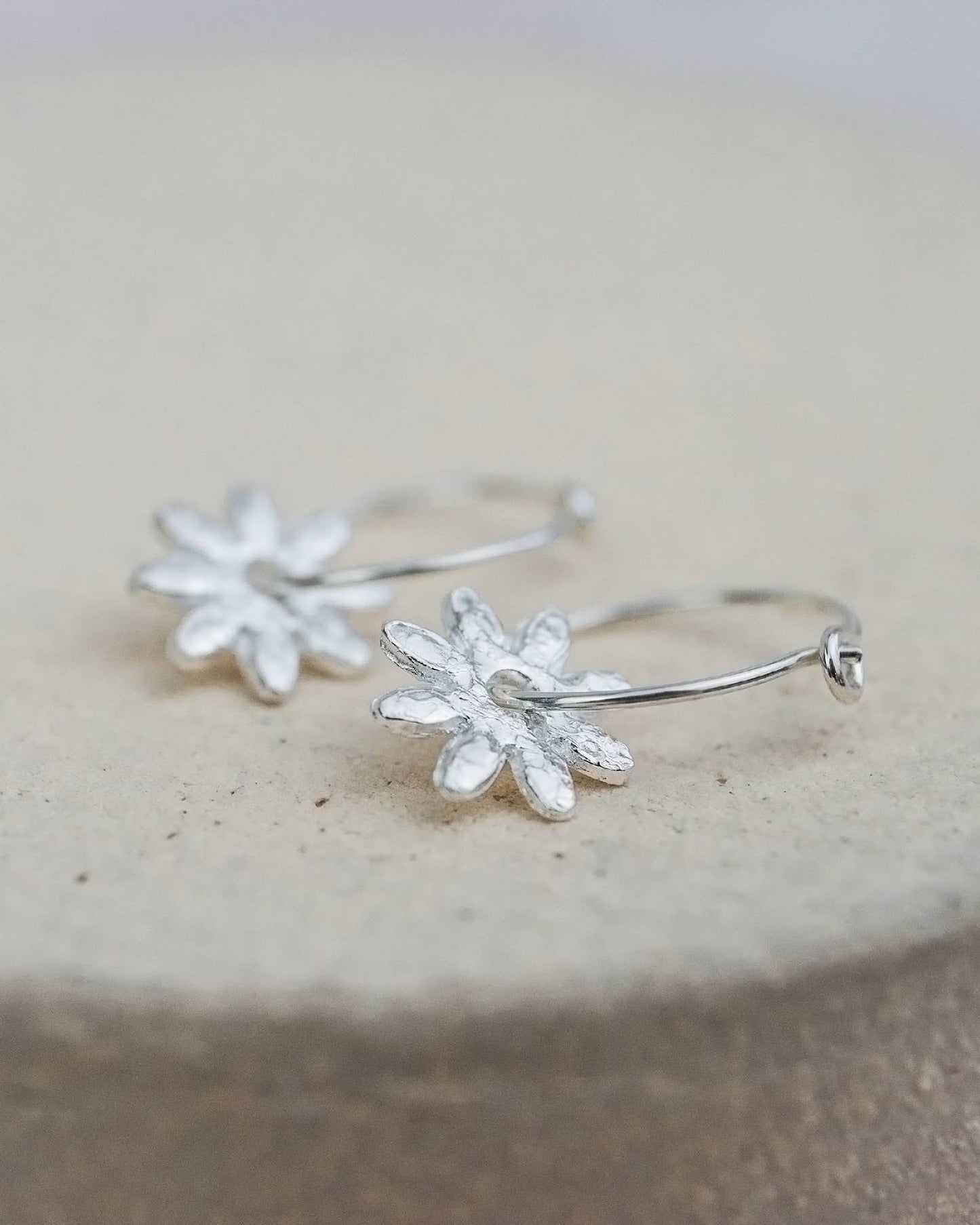 Silver floral hoop earrings on a stone surface