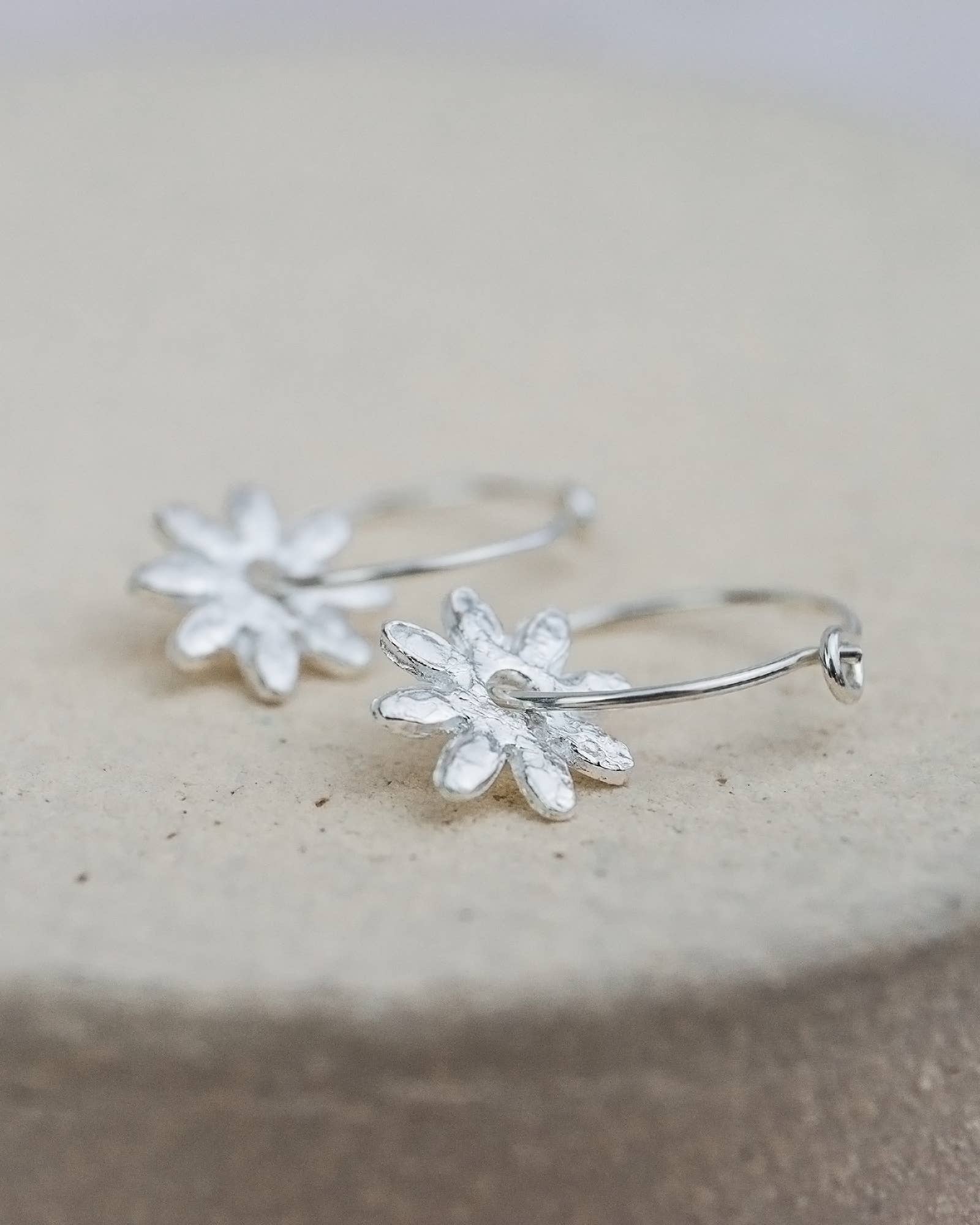 Silver floral hoop earrings on a stone surface
