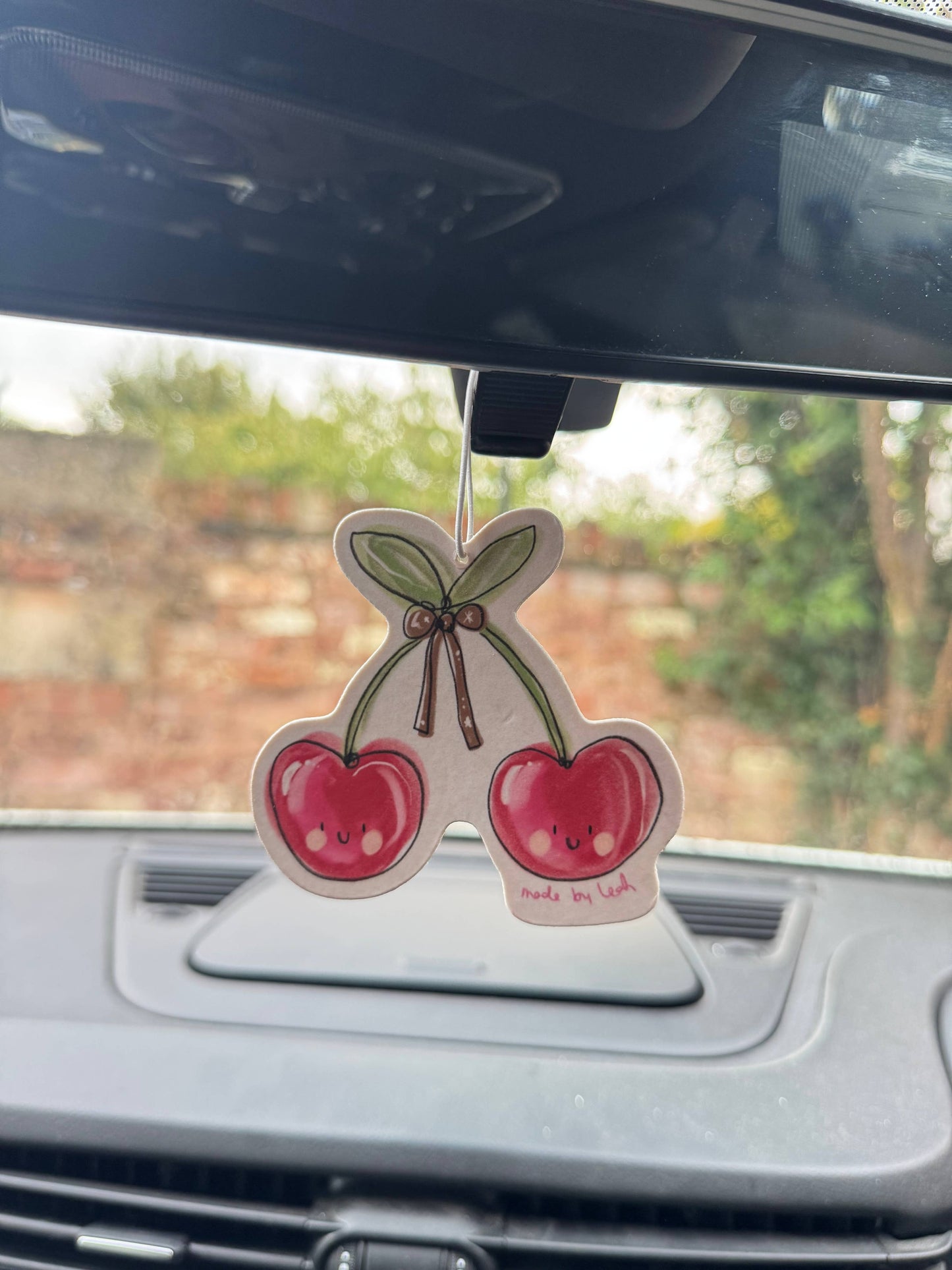 Cherry-themed car air freshener hanging from a car's rearview mirror.