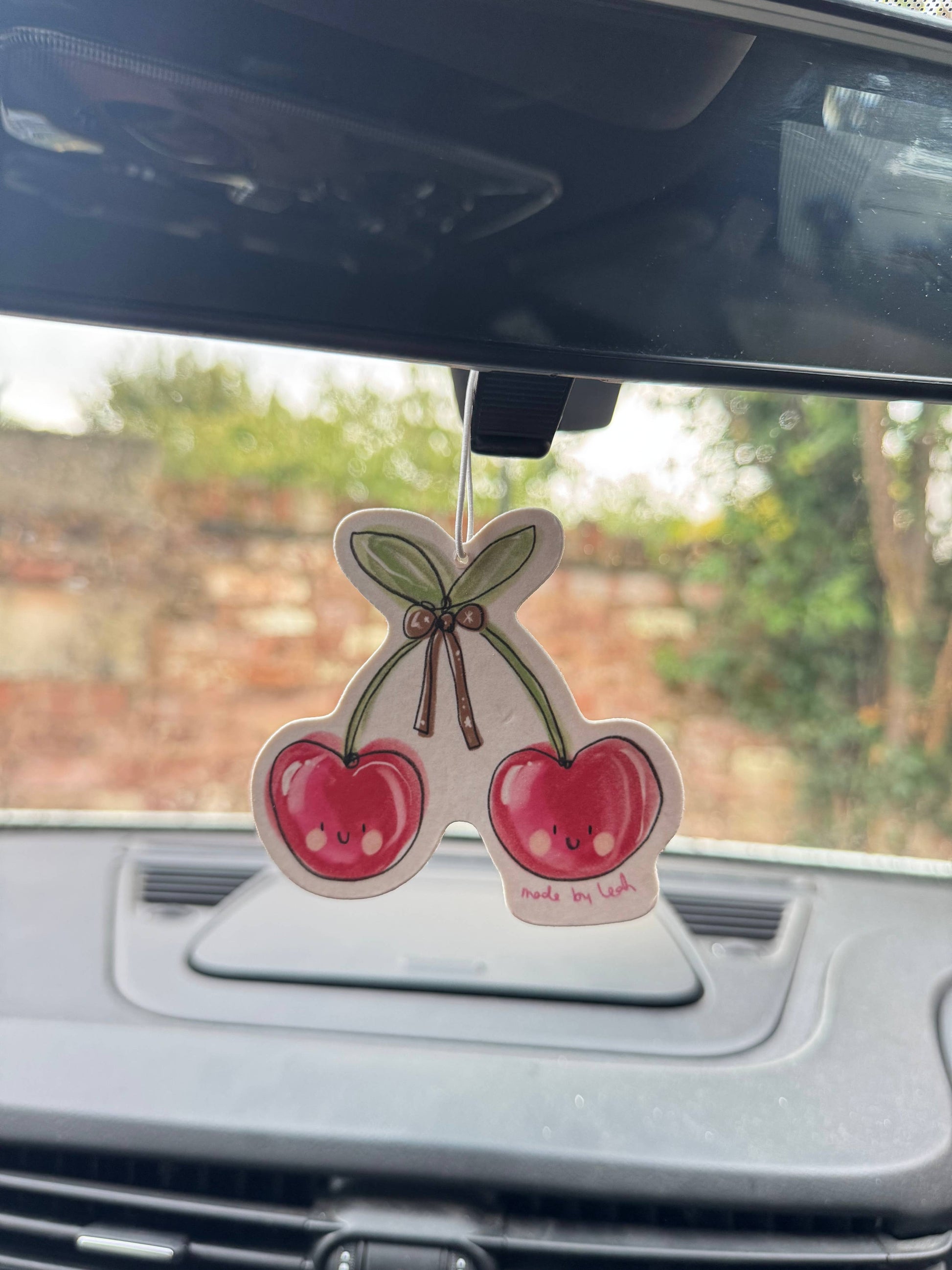 Cherry-themed car air freshener hanging from a car's rearview mirror.