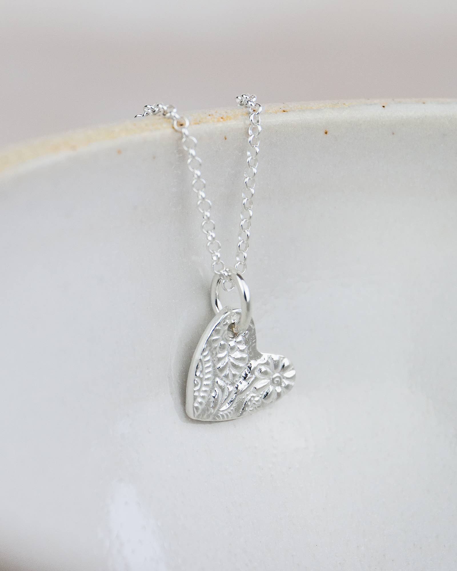 Silver necklace with a heart-shaped pendant on a white dish