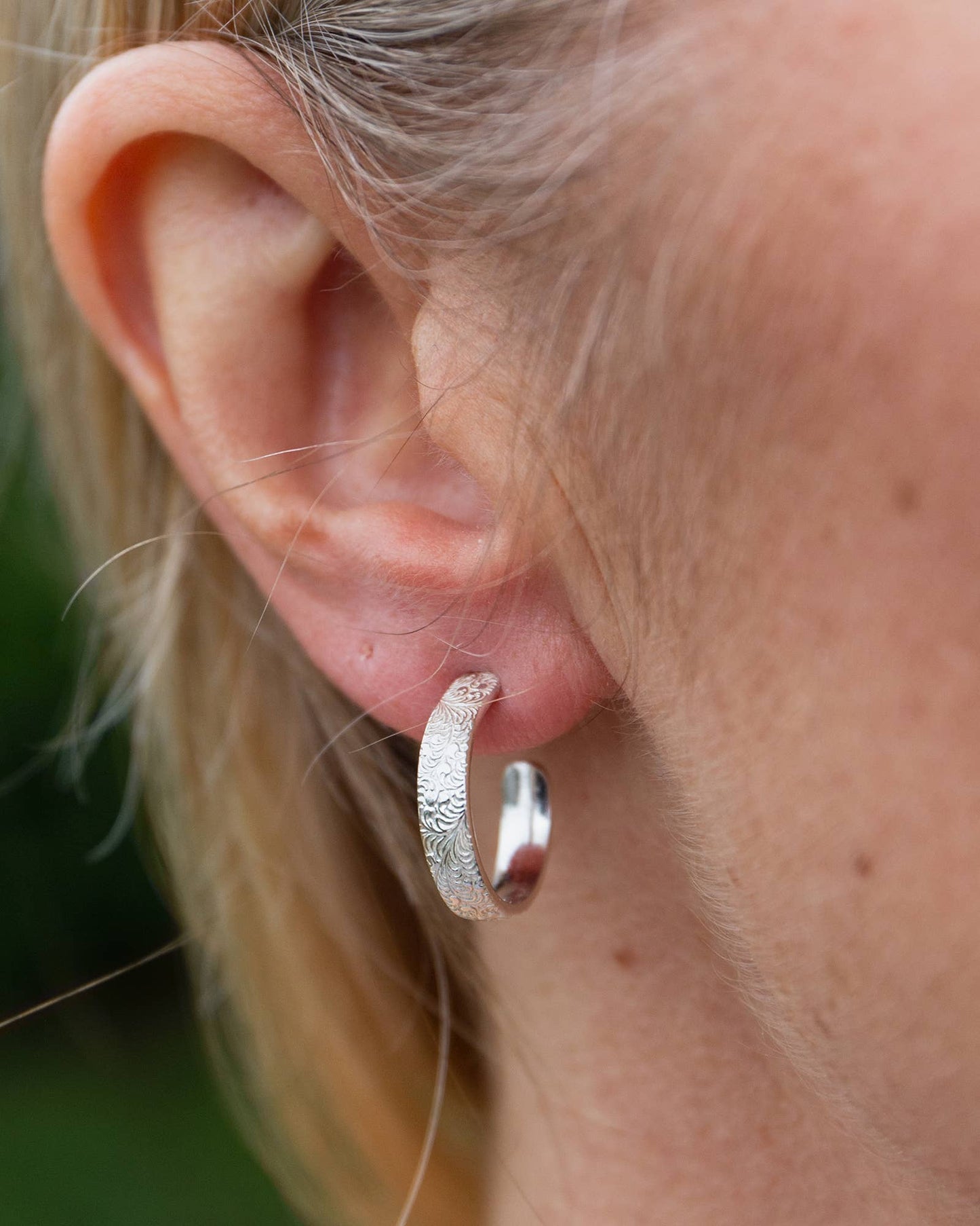 Silver hoop earring worn by a person with blonde hair.