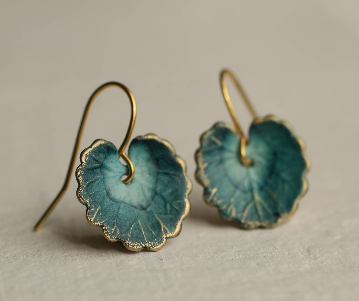 Teal ceramic earrings with gold hooks on a beige background