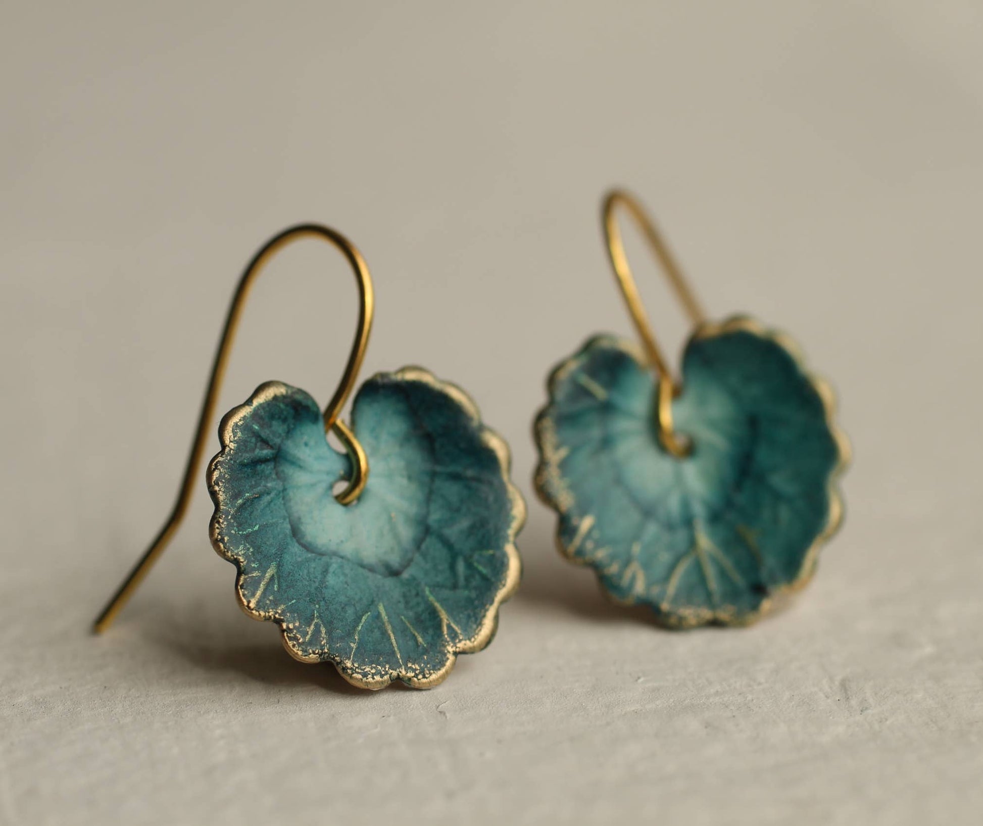 Teal ceramic earrings with gold hooks on a beige background
