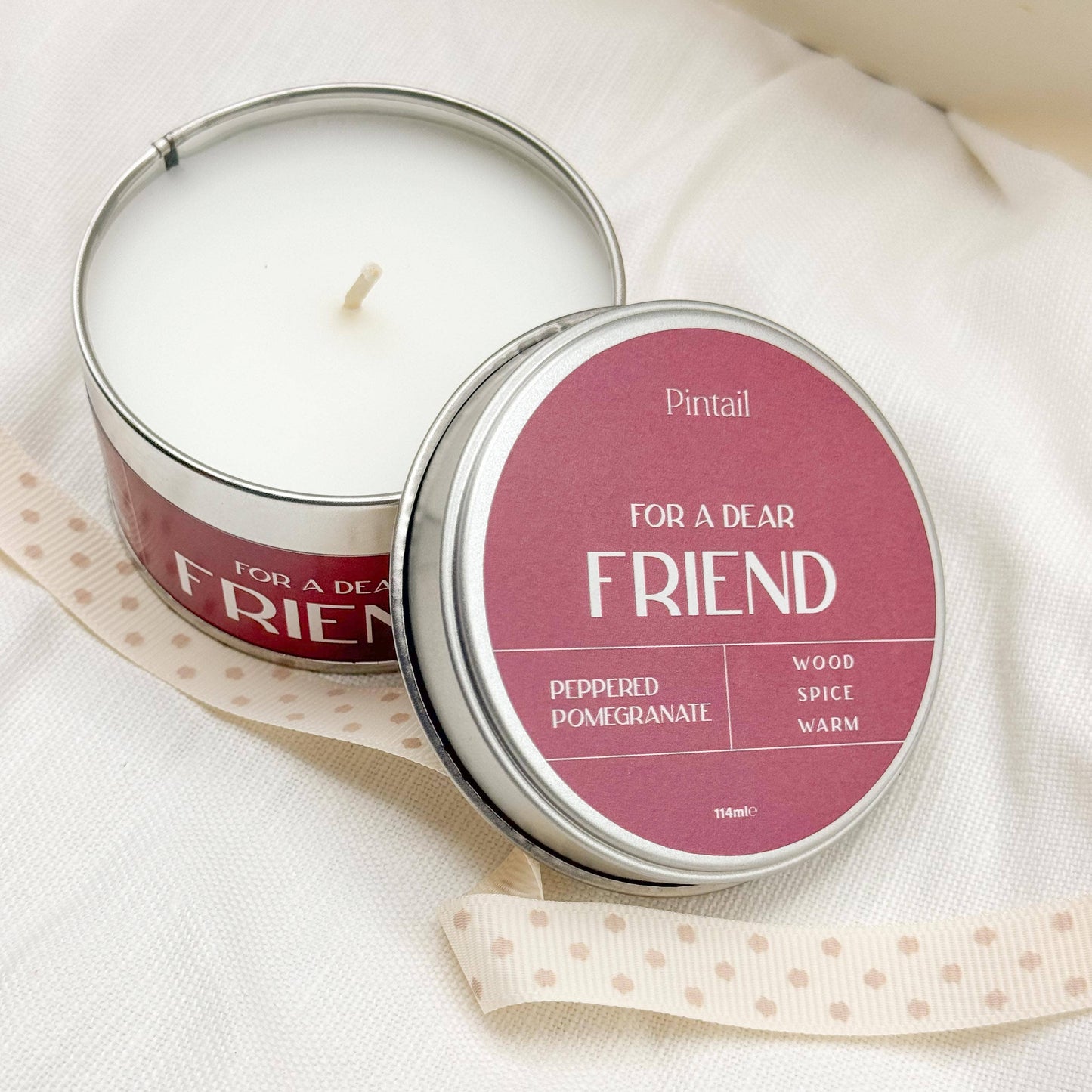 Candle in a tin labeled 'For a Dear Friend' by Pintail on a white fabric background