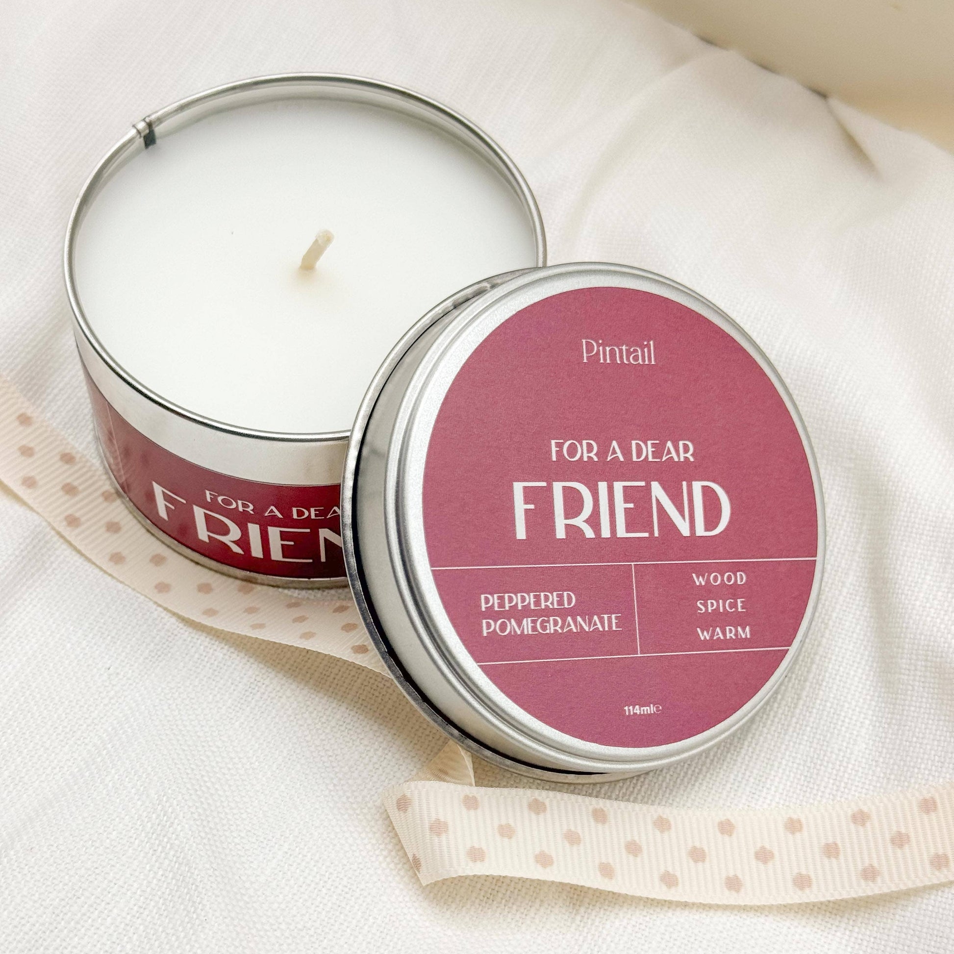 Candle in a tin labeled 'For a Dear Friend' by Pintail on a white fabric background