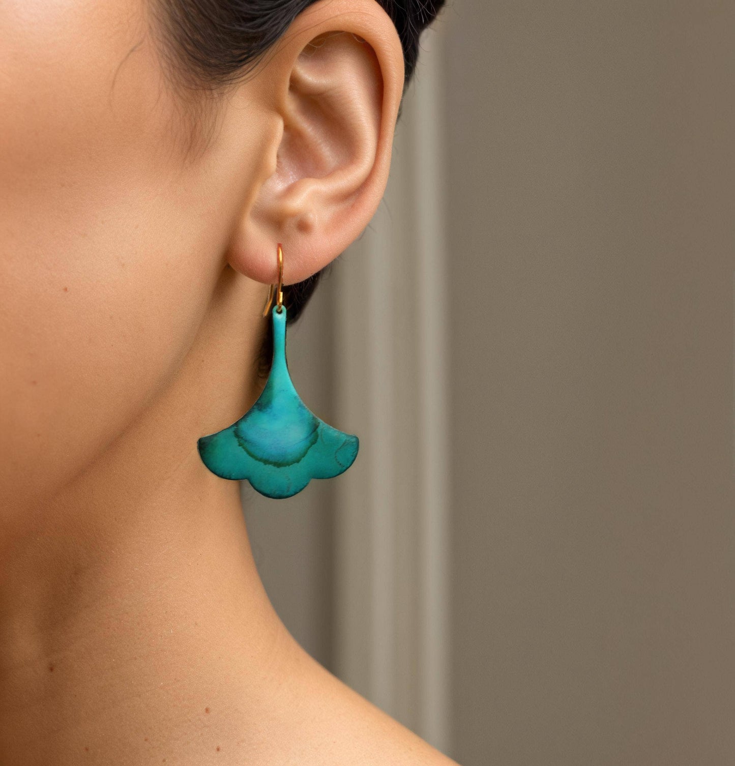 Turquoise leaf-shaped earring worn by a person against a neutral background