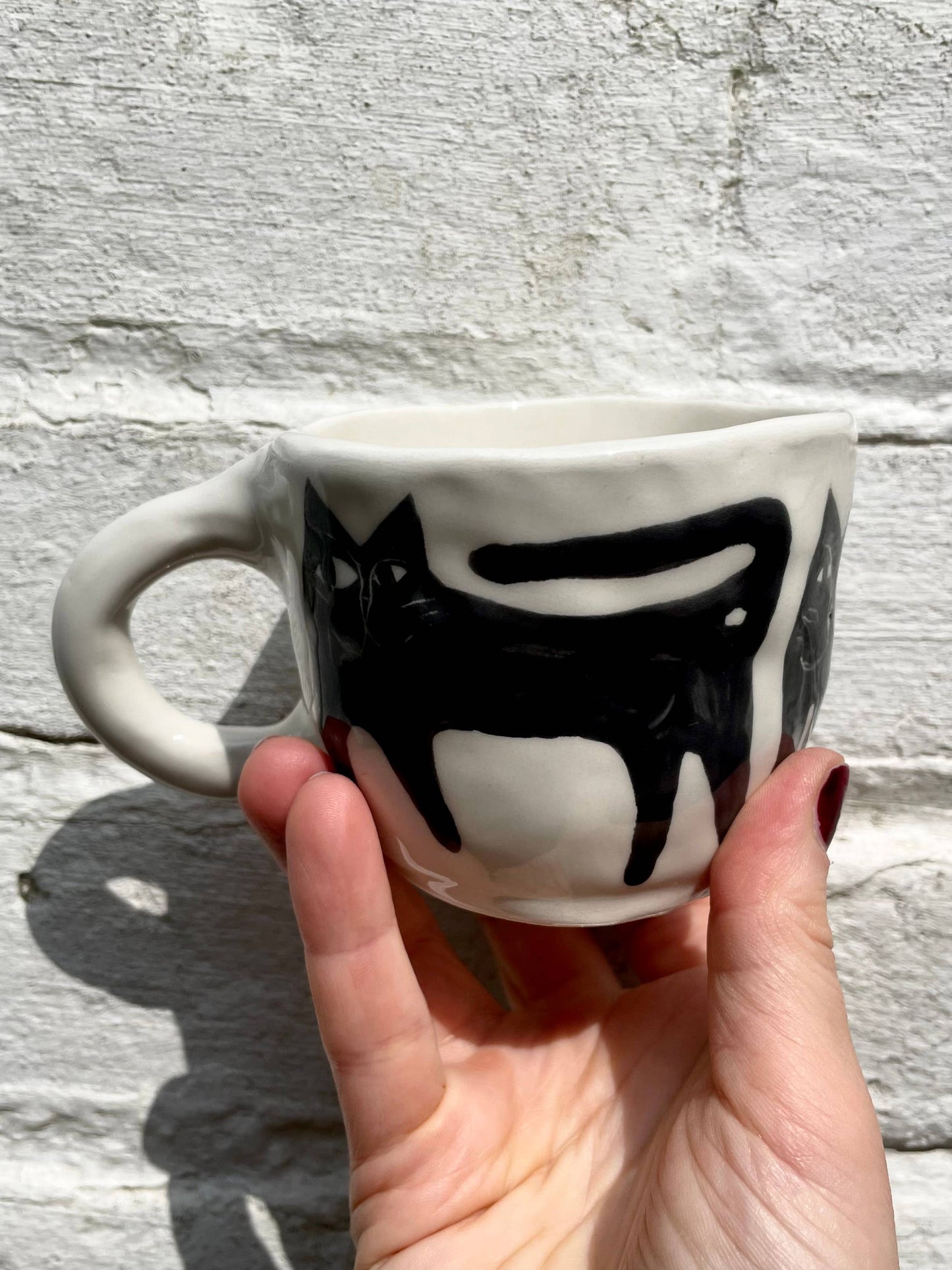 White mug with black cat design held by a hand against a light gray background