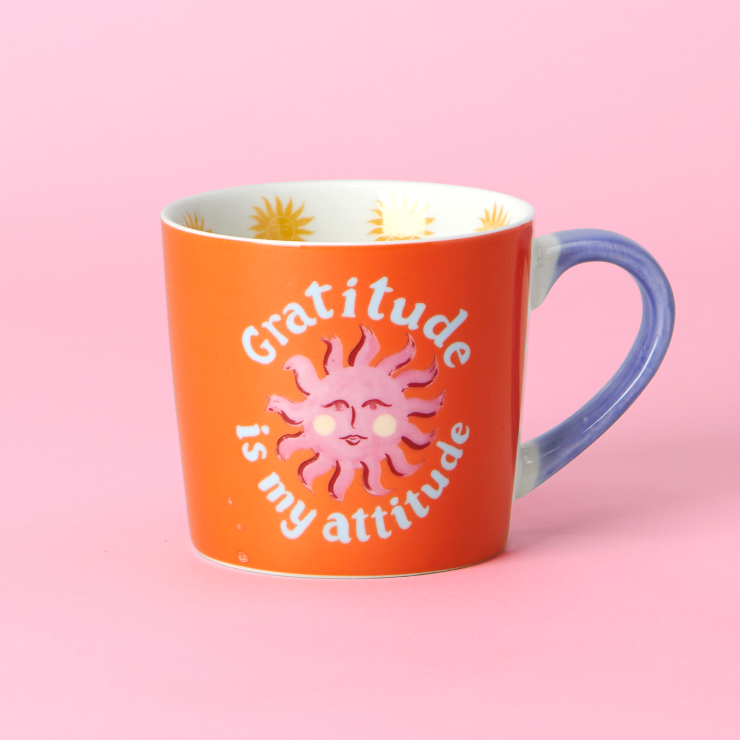 Orange mug with sun design and 'Gratitude is my attitude' text on a pink background