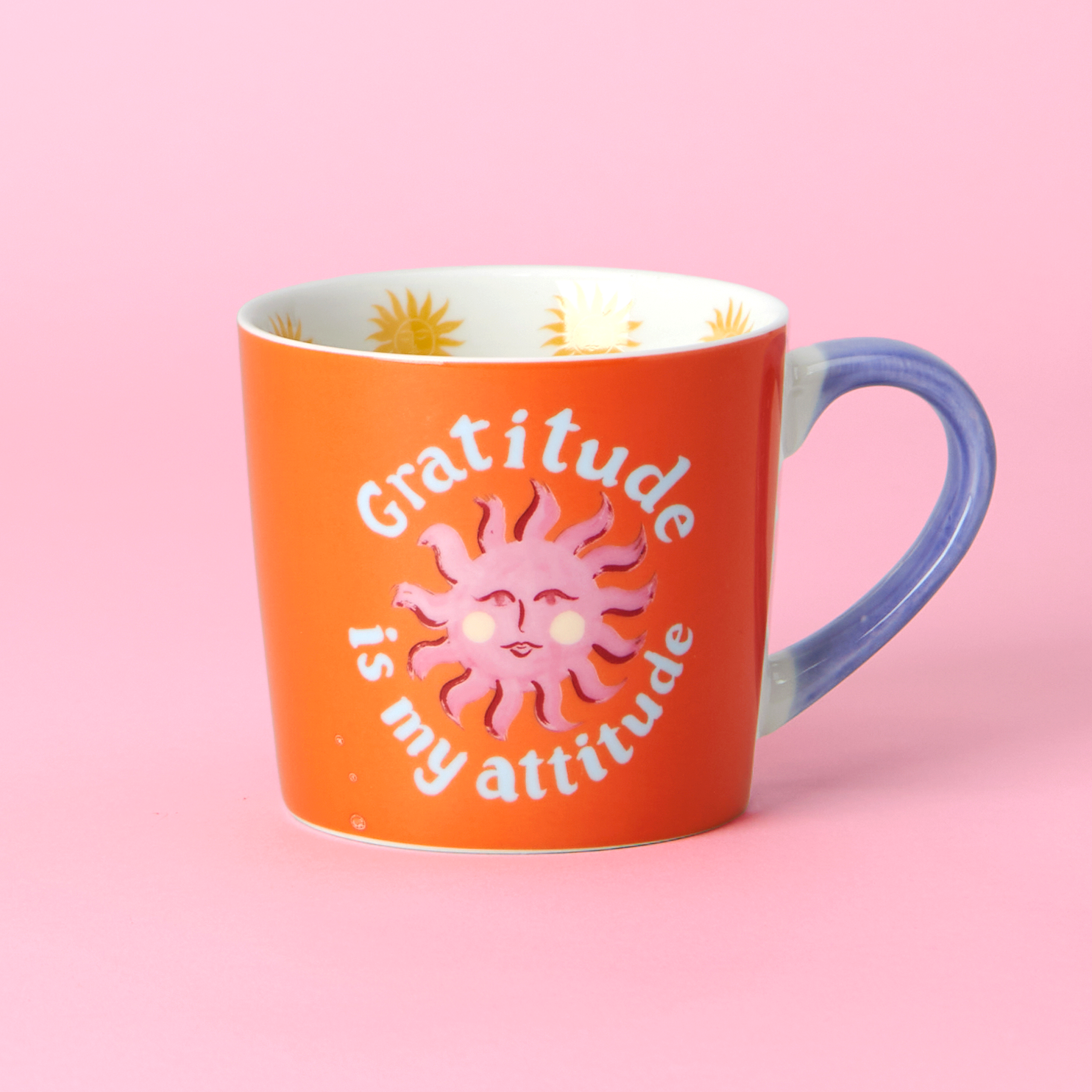 Orange mug with sun design and 'Gratitude is my attitude' text on a pink background