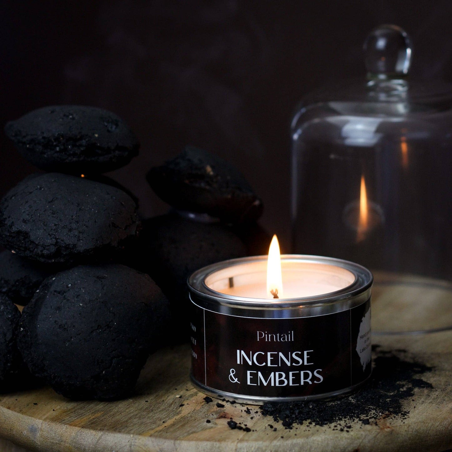 Candle labeled 'Incense & Embers' with black stones and a glass jar in the background