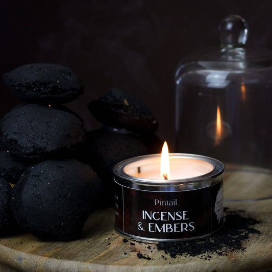 Candle labeled 'Incense & Embers' with black stones and a glass jar in the background