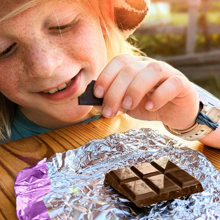 Child eating a chocolate bar with a piece of foil on a wooden surface