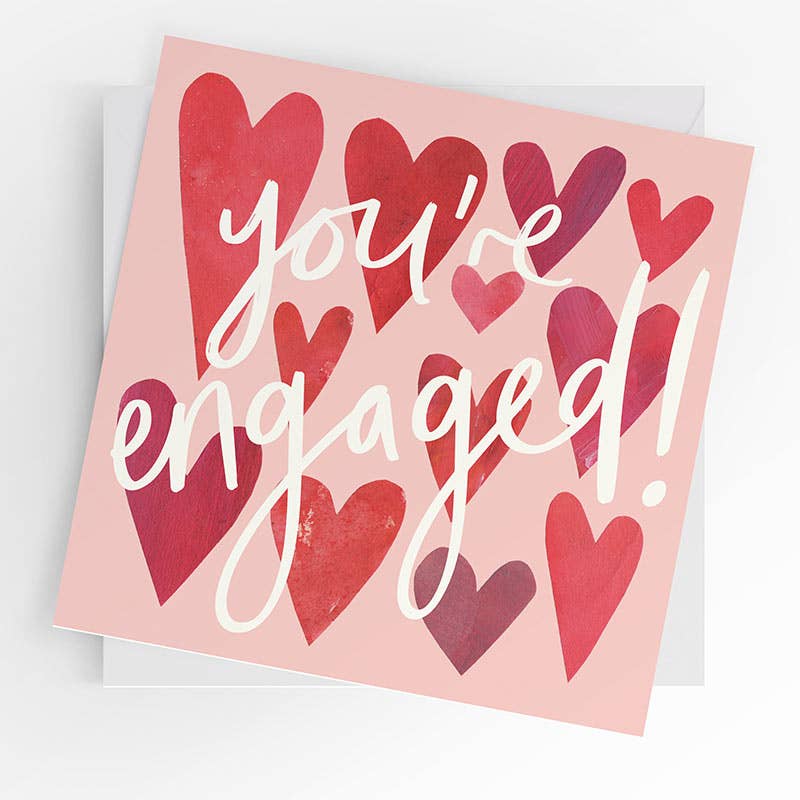 Card with red hearts and 'you're engaged!' text on a pink background