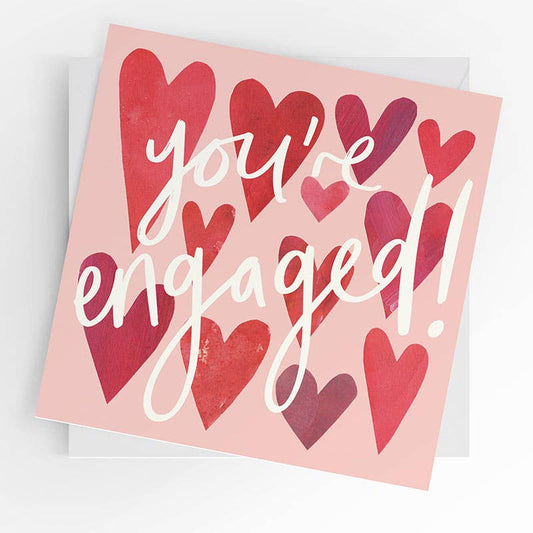 Card with red hearts and 'you're engaged!' text on a pink background
