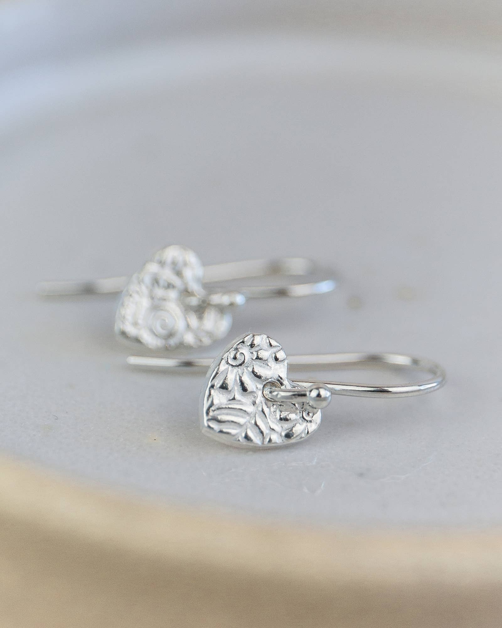 Silver heart-shaped earrings on a light gray background