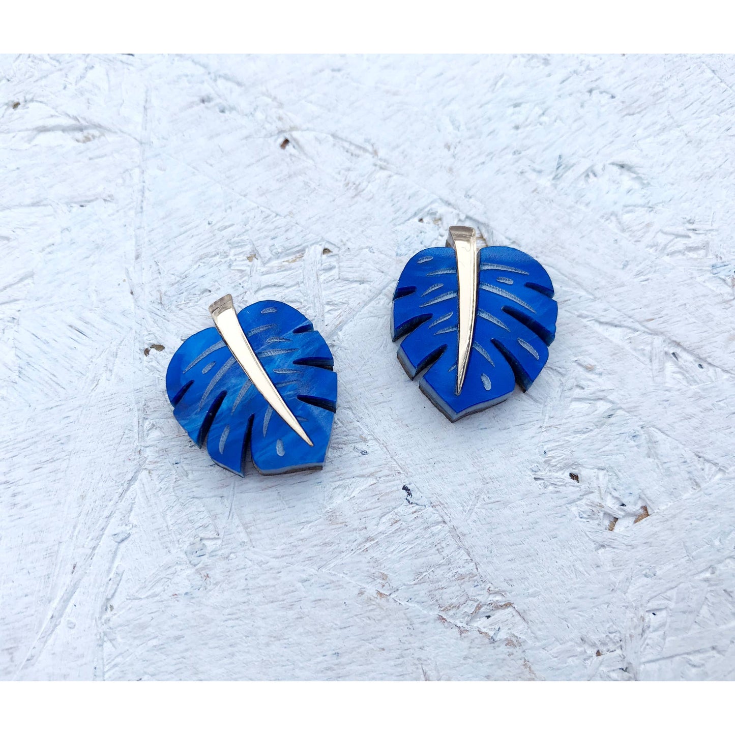 Blue leaf-shaped earrings with gold accents on a textured white surface