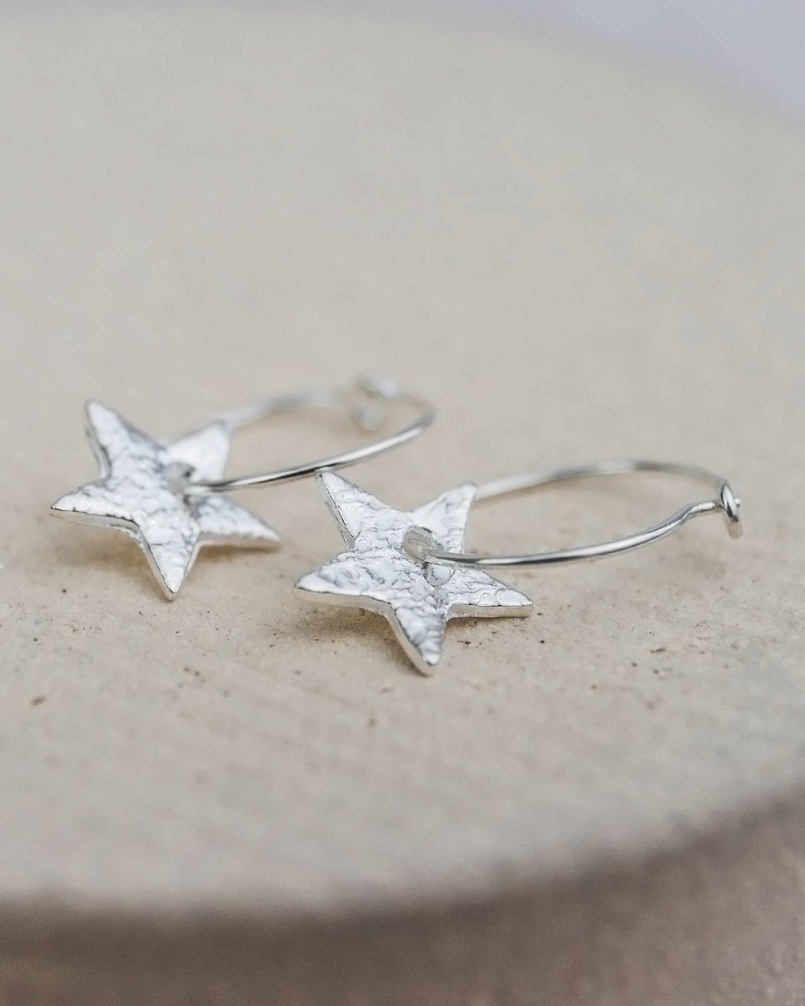 Silver star-shaped earrings on a beige surface