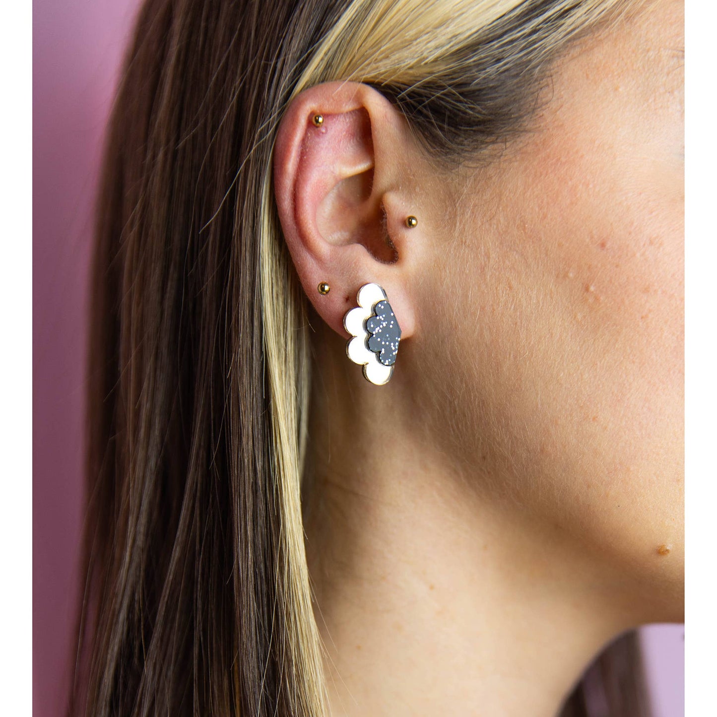 Close-up of a person wearing a floral earring with a pink background