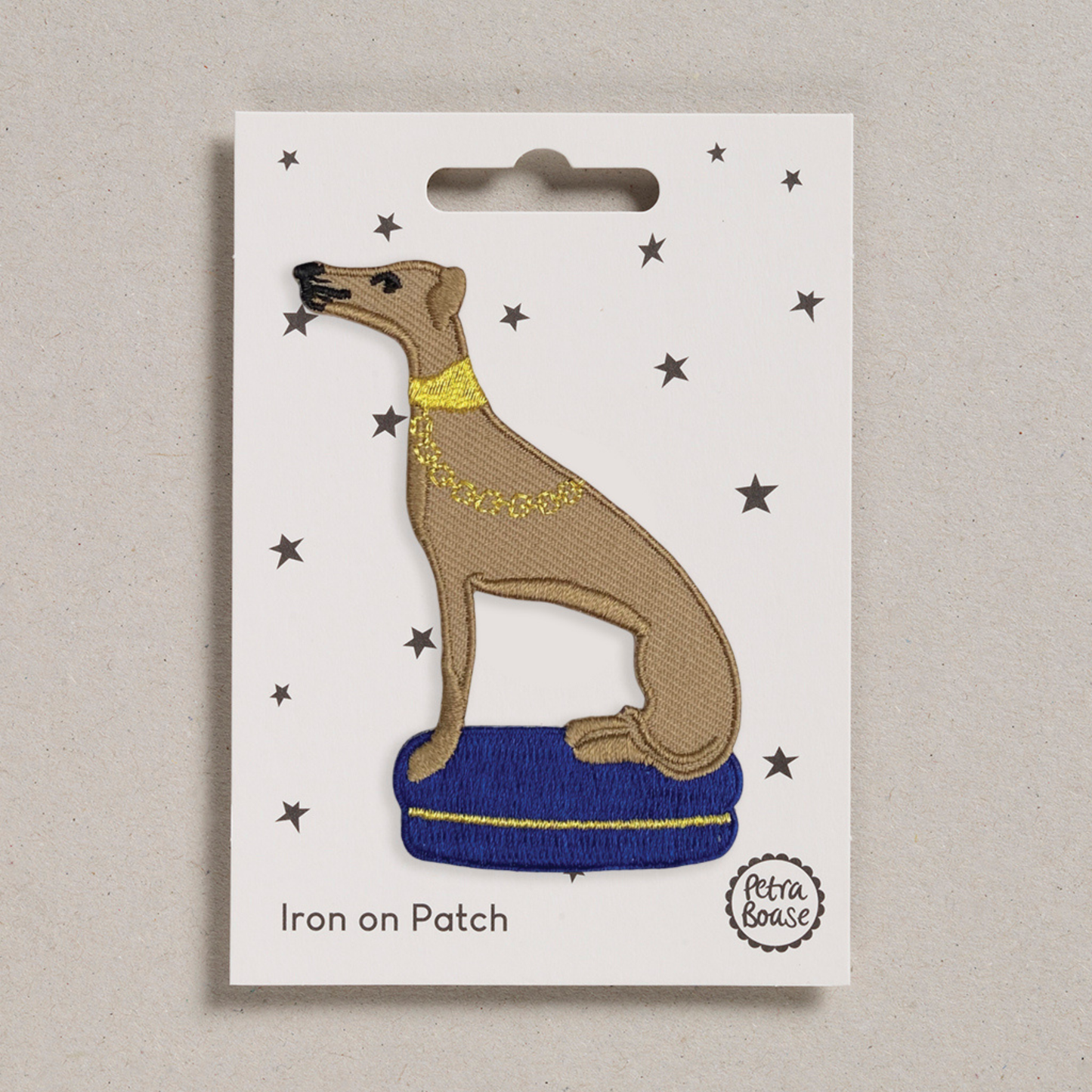 Iron on patch of a dog with a blue cushion on a white card with star patterns, brand 'Petra Boase' visible.
