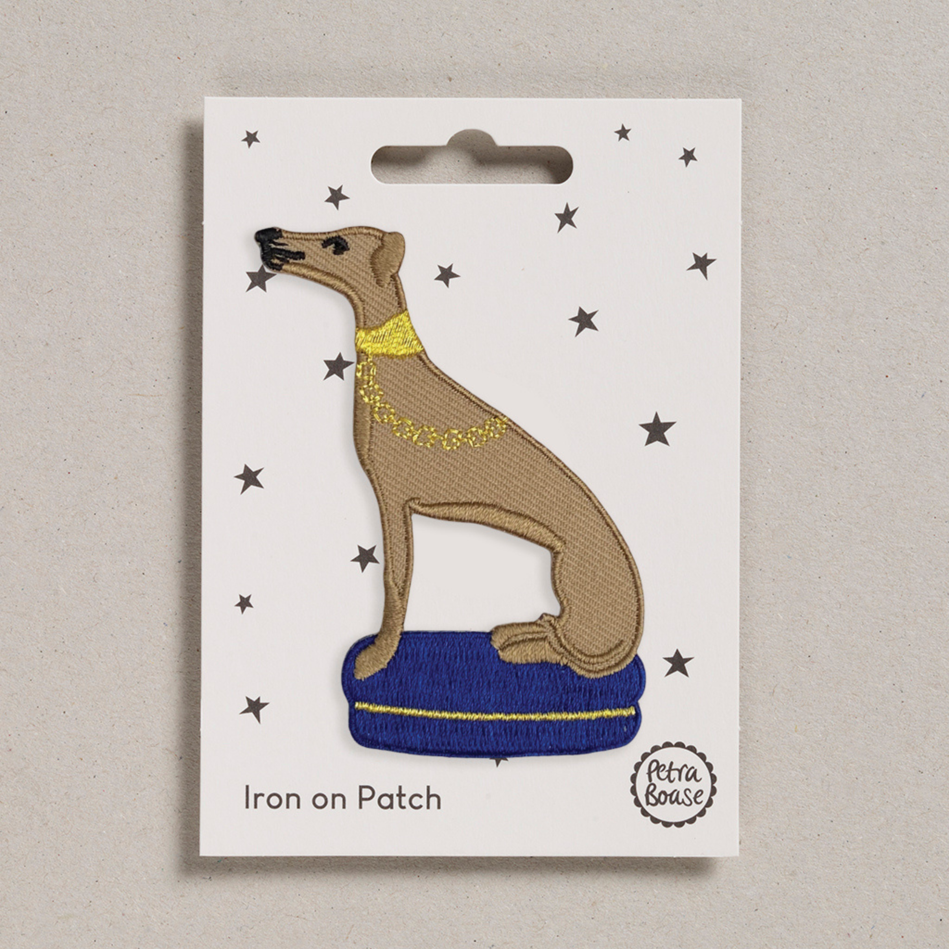 Iron on patch of a dog with a blue cushion on a white card with star patterns, brand 'Petra Boase' visible.