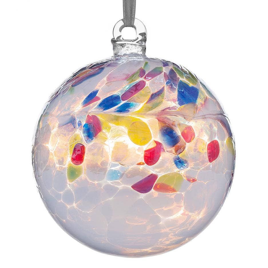 A clear glass Christmas ornament ball with a colorful mosaic pattern of red, blue, yellow, green, and purple glass pieces, hanging from a silver ribbon on a white background.