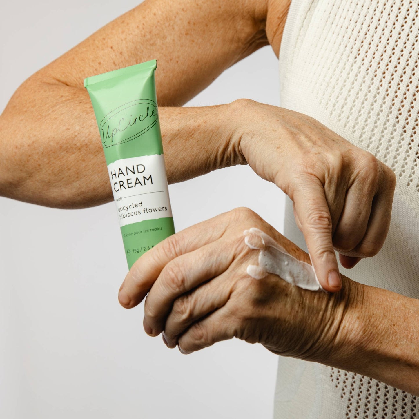 Person applying hand cream to their hand with a green tube labeled 'Hand Cream' in the foreground.