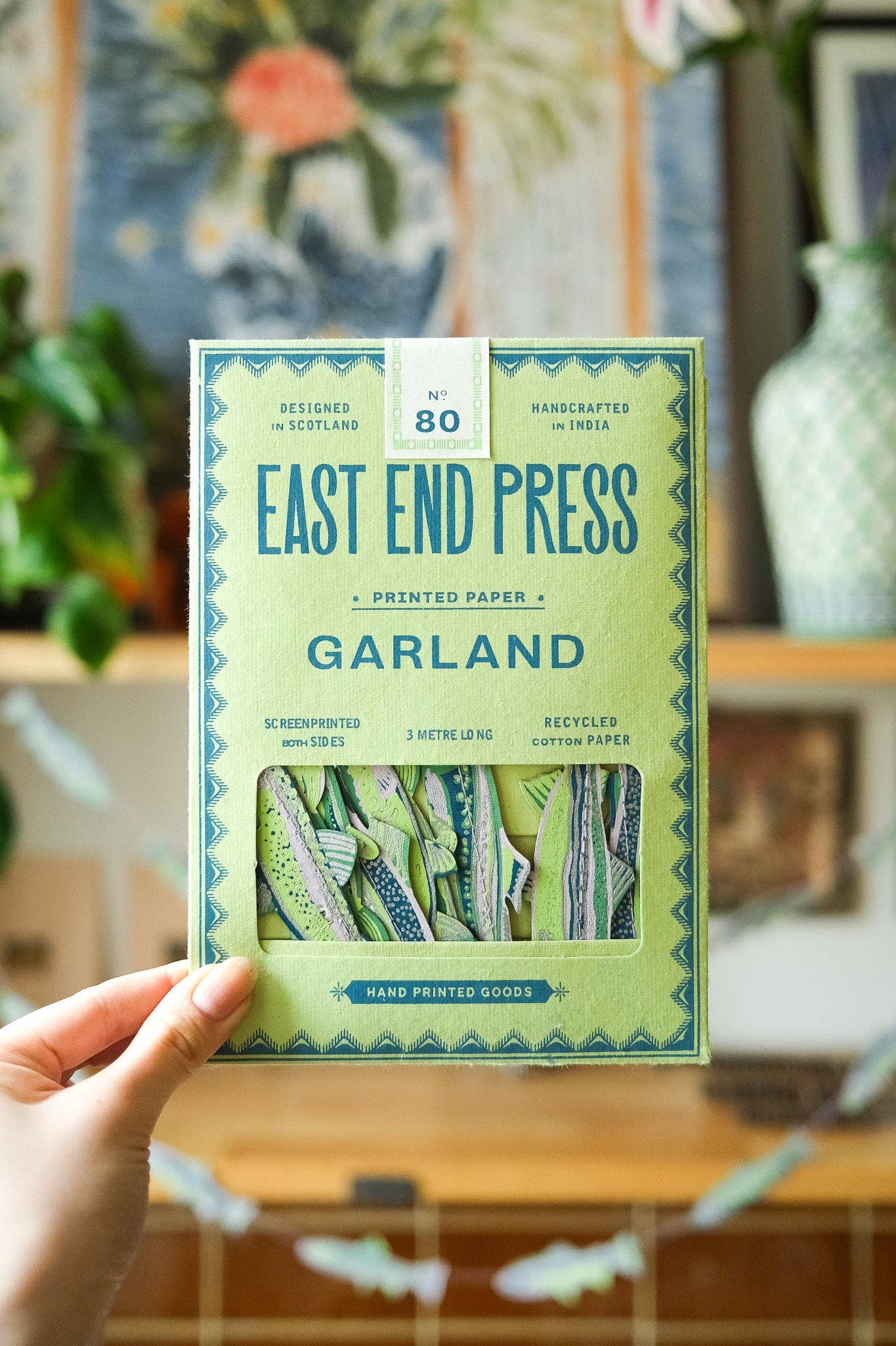 Handheld package of East End Press Garland printed paper with a blurred indoor setting in the background.