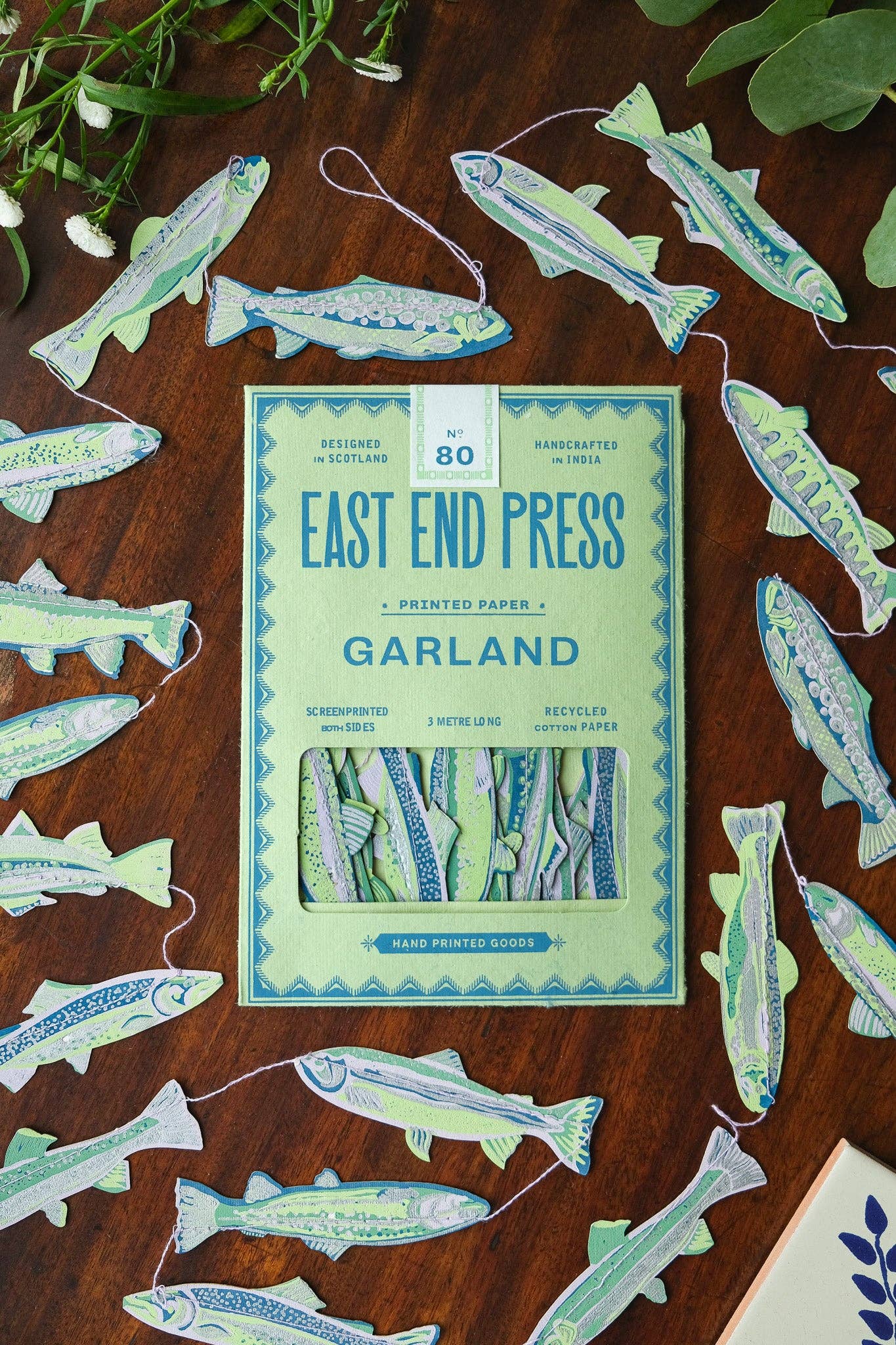 Packaging of East End Press Garland with paper fish decorations on a wooden surface.