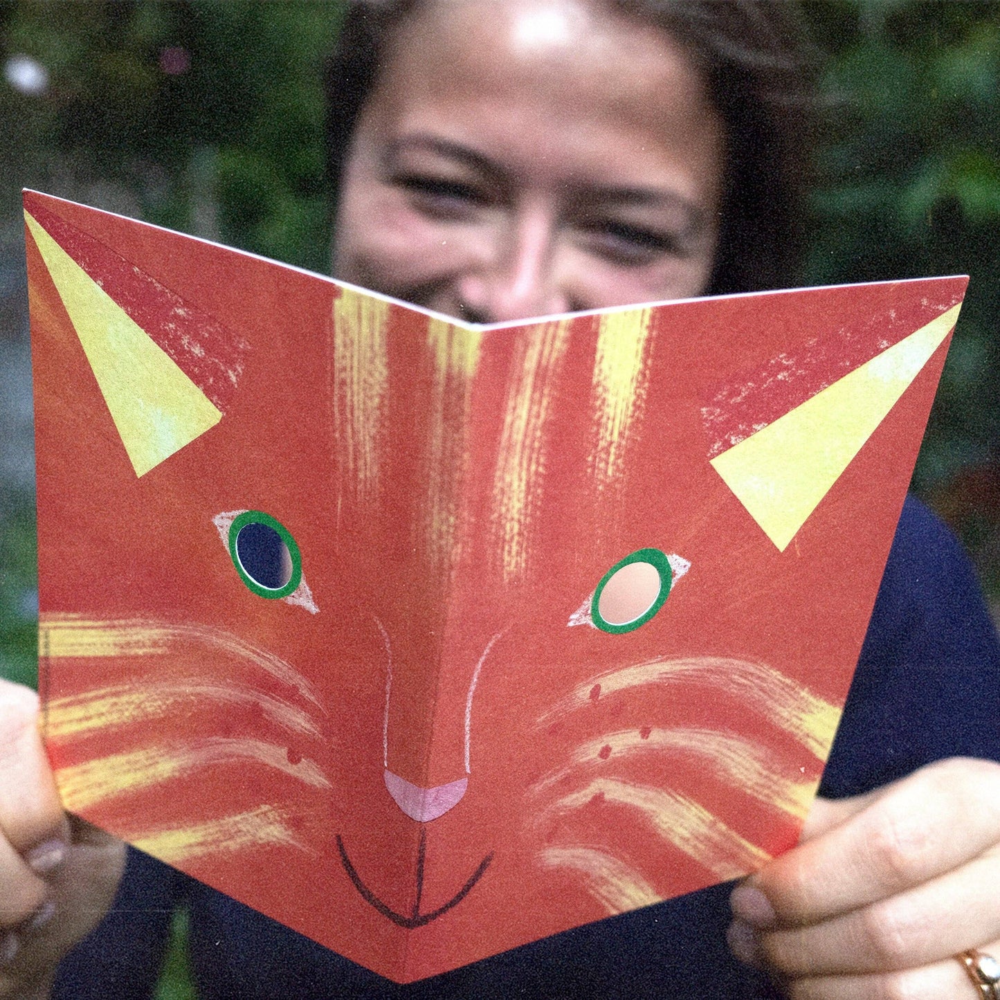 Person holding a red card with a cat design in front of their face