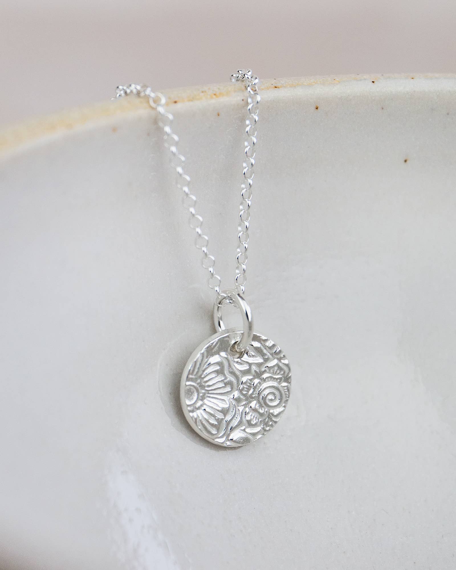 Silver necklace with a detailed pendant on a light background