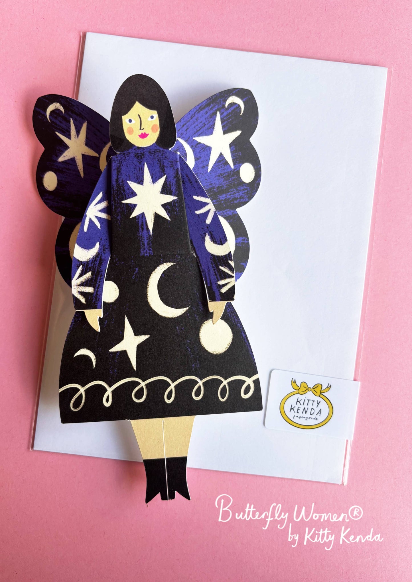 Butterfly-shaped paper doll with star and moon designs on a pink background