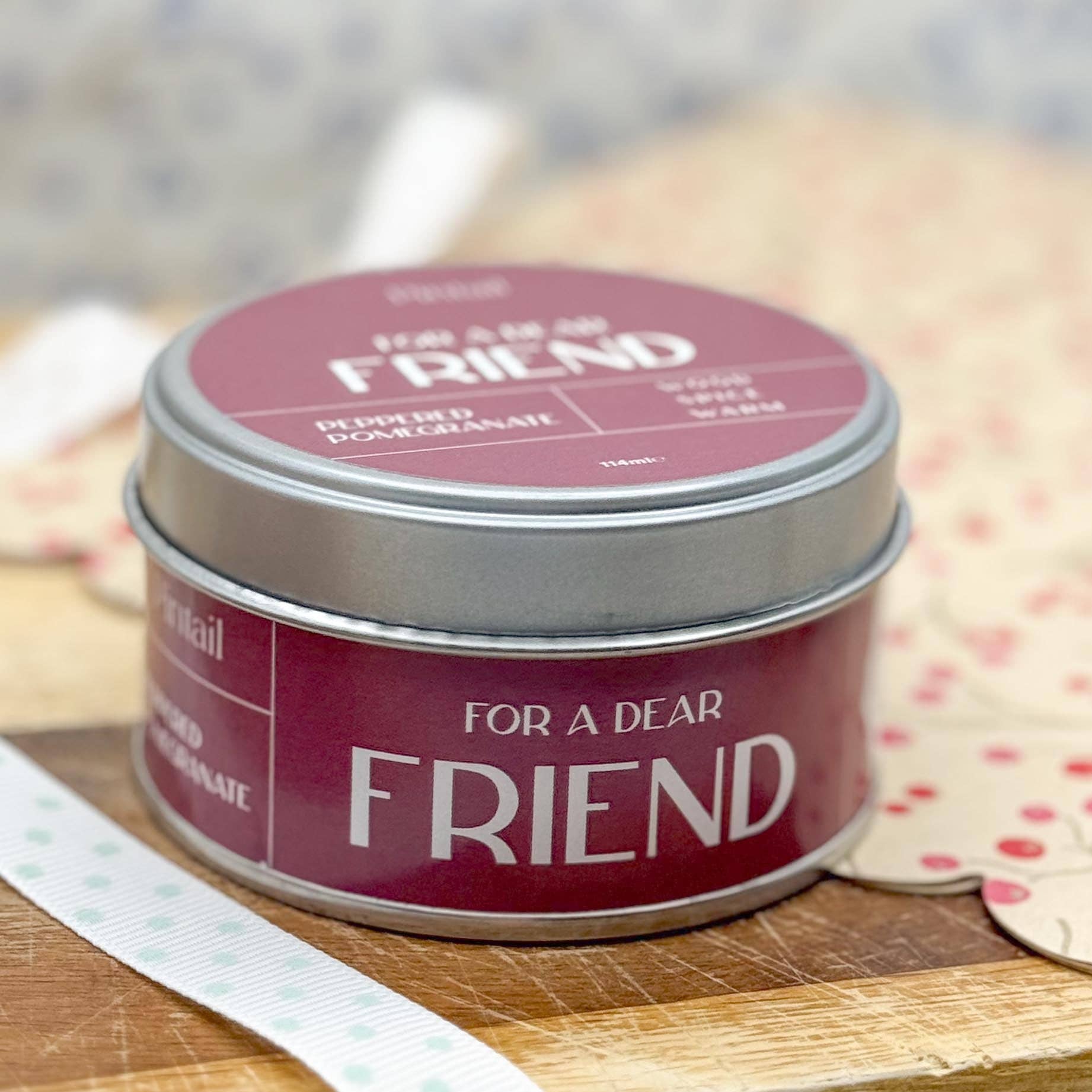 Candle tin labeled 'For a Dear Friend' on a wooden surface with a blurred background