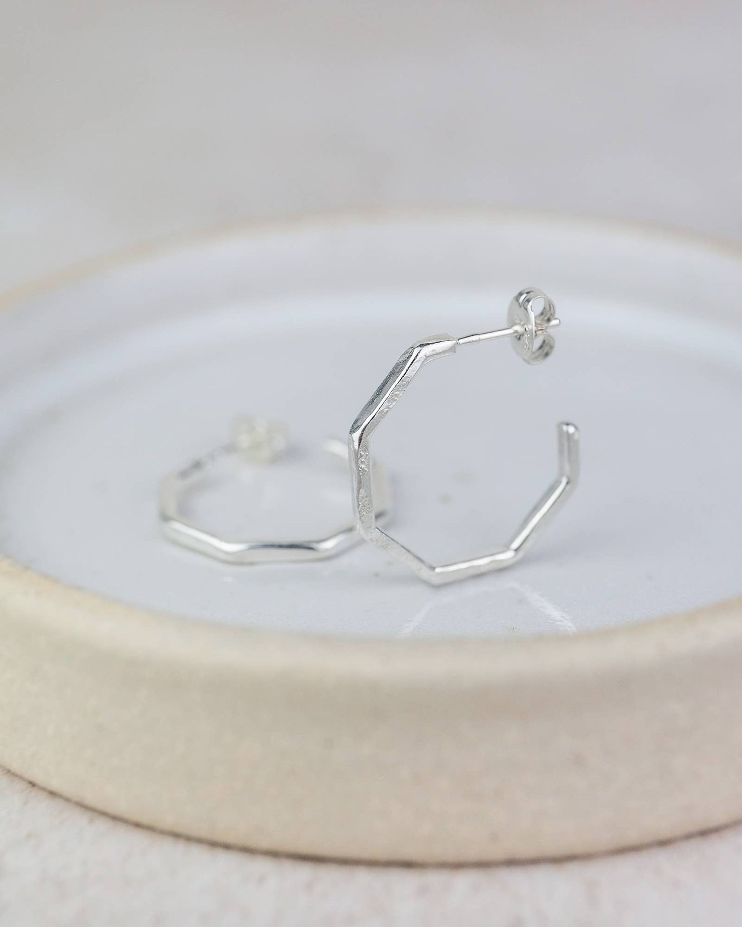 Silver hexagonal hoop earrings on a white dish with a beige rim.