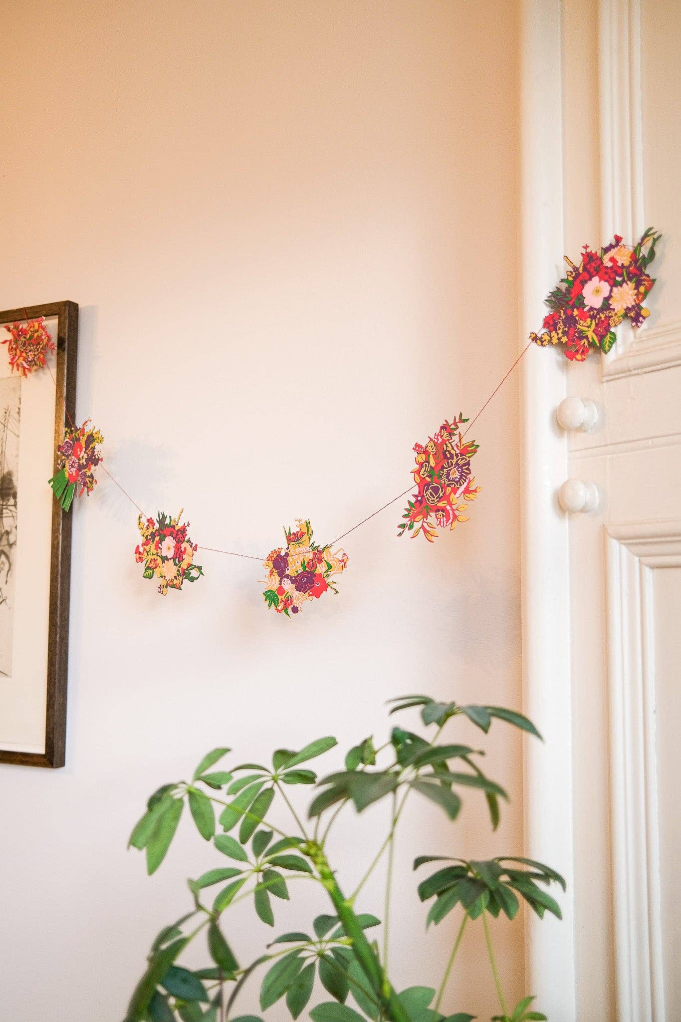 Floral garland hanging on a wall with a plant in the foreground