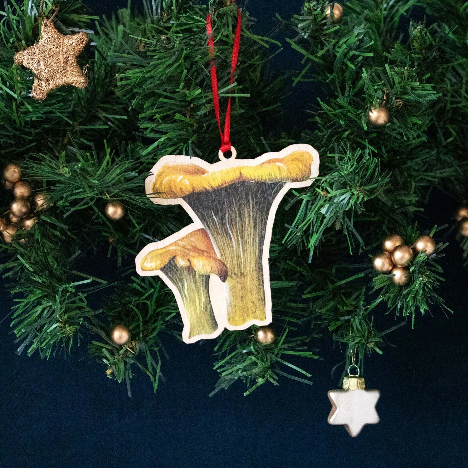 A wooden Christmas decoration of a Chanterelle mushroom, threaded with a bright red ribbon.