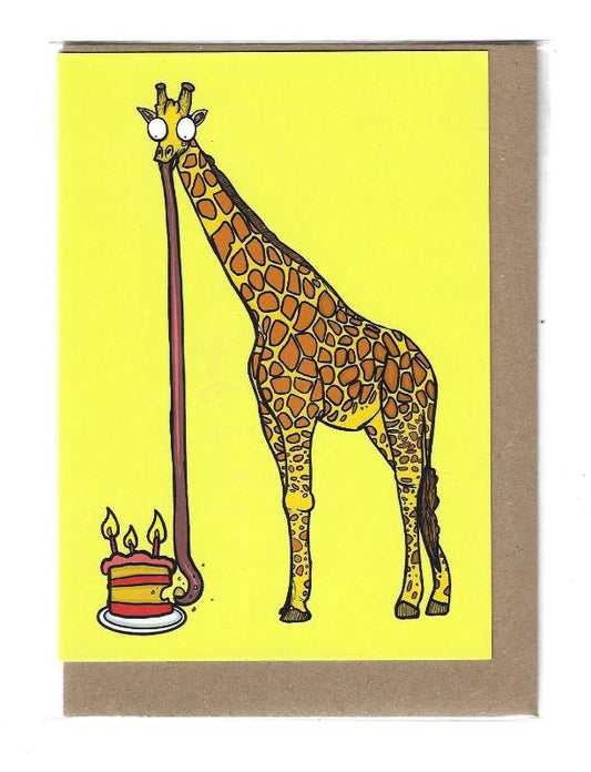 A giraffe with a long tongue eats a cake on the ground.